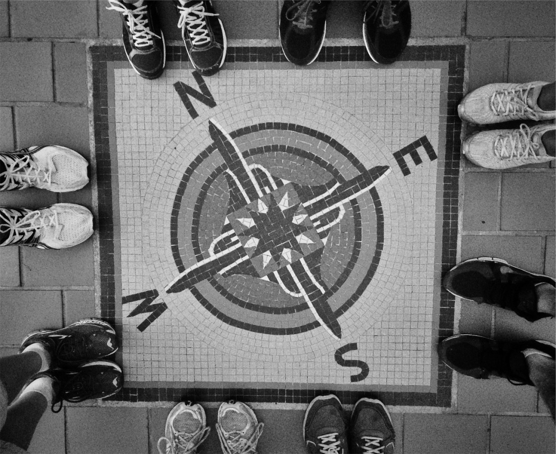 black and white image of a compass painted on the floor with , N, S , E , W with  two sets on feet on each one